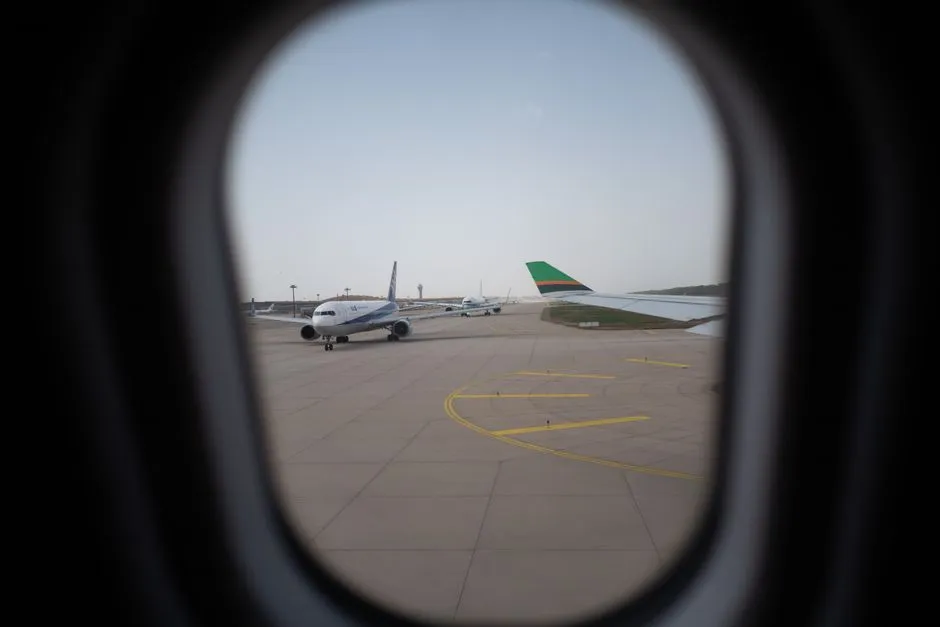 Airplanes on an airport runway seen through a terminal window, illustrative photo